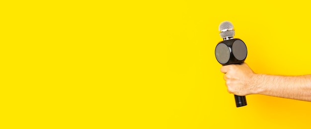 La mano del hombre sostiene un micrófono en un agujero en un banner de fondo amarillo brillante roto