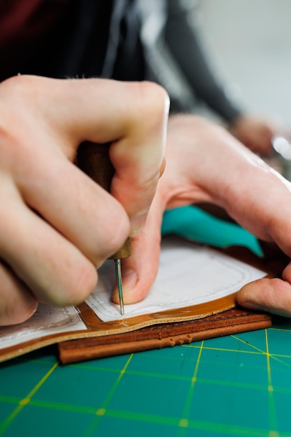 La mano de un hombre sostiene piezas de cuero para una billetera de cuero en su taller El proceso de trabajar con cuero marrón natural El artesano sostiene el oficio