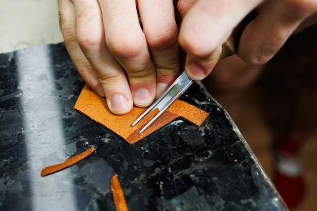 La mano de un hombre sostiene piezas de cuero para una billetera de cuero en su taller El proceso de trabajar con cuero marrón natural El artesano sostiene el oficio