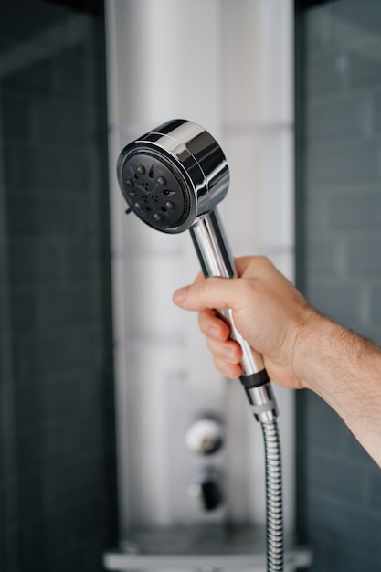 La mano de un hombre sostiene la regadera de la ducha. Fontanería moderna para el baño y la ducha.