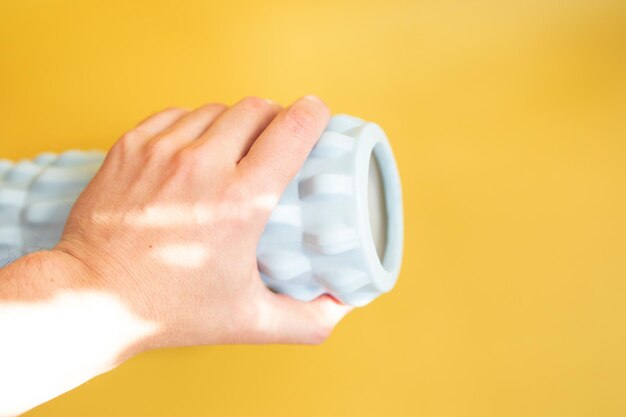 La mano del hombre sostiene un rollo de masaje azul claro sobre un fondo amarillo