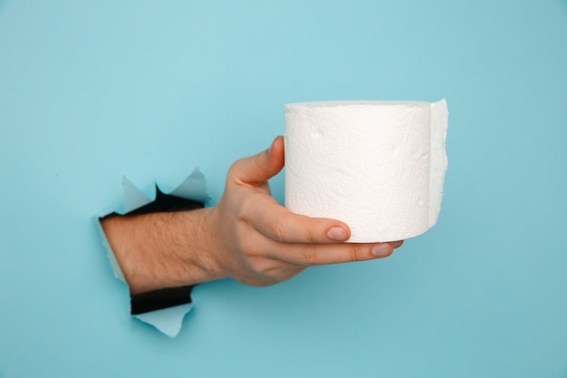 La mano del hombre sostiene un rollo de papel higiénico en una pared azul