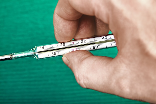 La mano del hombre sostiene un termómetro de mercurio para el cuerpo, cuya escala muestra una temperatura de 39 grados.