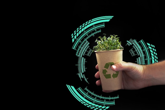 La mano de un hombre sostiene un vidrio ecológico con una planta verde en un espacio en blanco de fondo negro para un texto inteligente