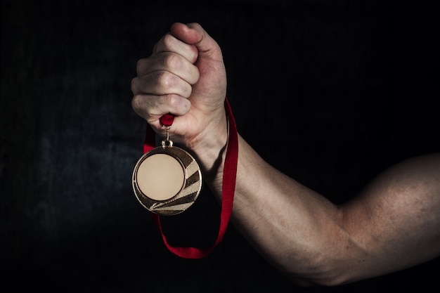 La mano de un hombre sucio tiene una medalla de oro sobre un fondo oscuro. El concepto de éxito.