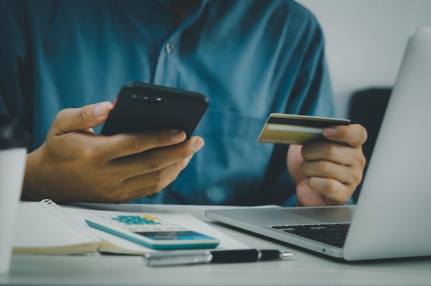 Mano de hombre con tarjeta de crédito y teléfono móvil, compras en línea, comercio electrónico y banca por Internet en el escritorio