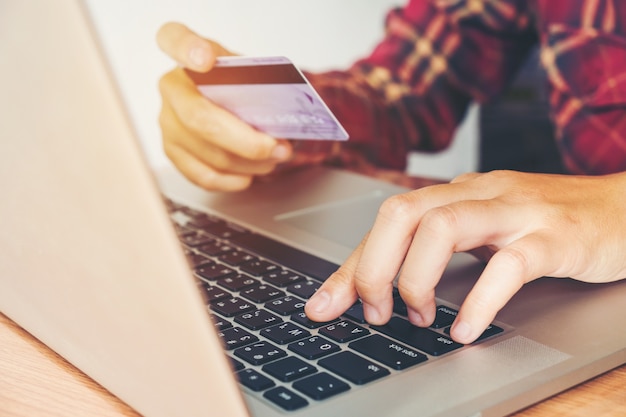 Mano de hombre con tarjeta de crédito usando teclado portátil en línea