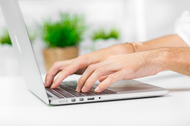 Mano del hombre en el teclado del ordenador portátil con monitor de pantalla en blanco de cerca