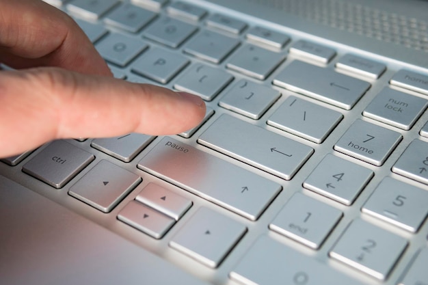 La mano del hombre en el teclado del portátil sobre un fondo claro presiona el botón de entrada en el teclado gris del ultrabook moderno