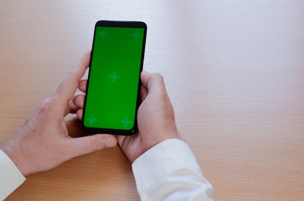 Mano del hombre con teléfono inteligente móvil con pantalla verde.