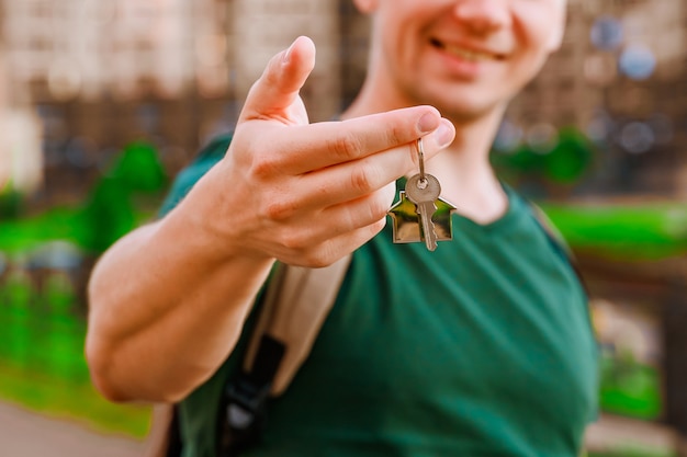 La mano de un hombre tiene las llaves de una nueva casa con el telón de fondo de edificios de gran altura