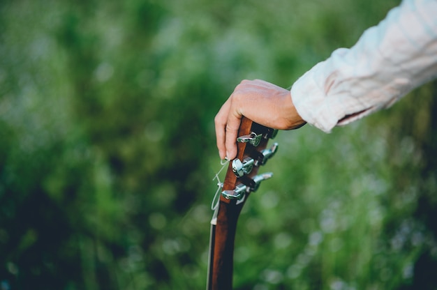 La mano del hombre toca la guitarra acústica, toca la guitarra solo en el jardín