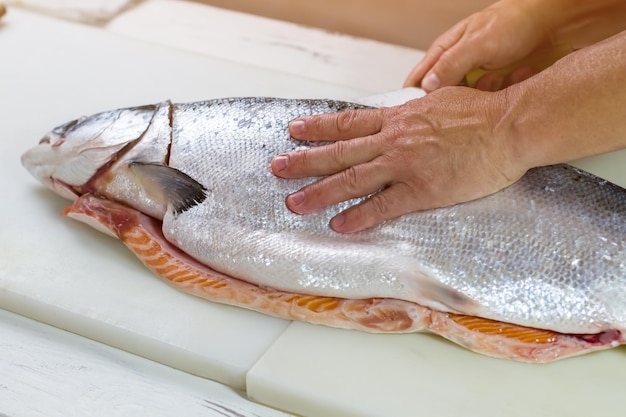 La mano del hombre toca el pescado crudo. El cuchillo corta peces grandes. Salmón fresco a bordo de cocción. Producto de calidad del supermercado.