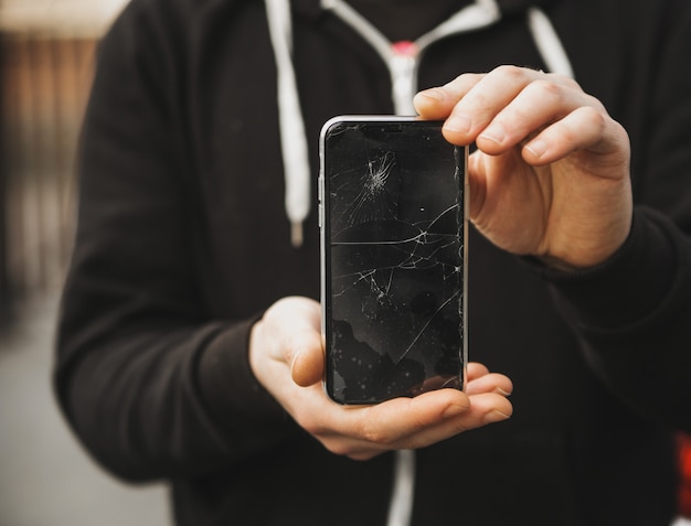 La mano del hombre toma roto dañado teléfono inteligente de asfalto