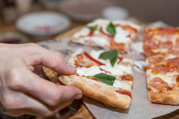 La mano de un hombre toma un trozo de pizza apetitosa en un café Comida rápida italiana Primer plano