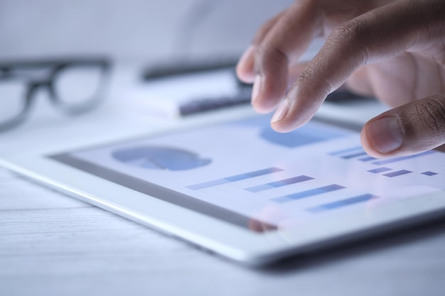 La mano del hombre trabajando en una tableta digital en el escritorio de la oficina usando un gráfico creado por uno mismo.