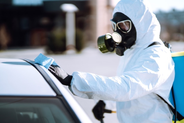 Mano de hombre en traje protector de lavado y desinfección asas de un coche.