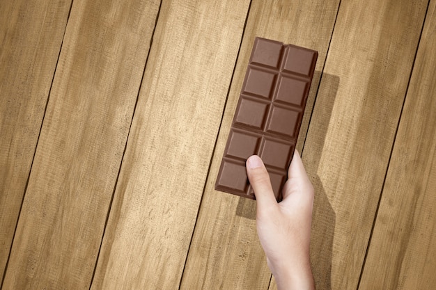 Mano humana con la barra de chocolate con fondo de tabla