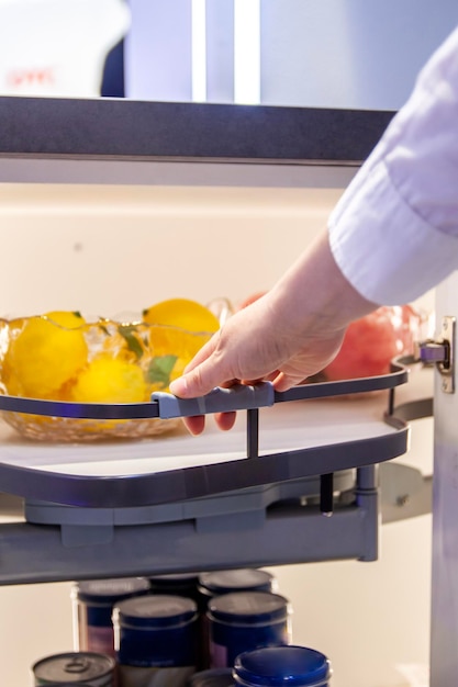 La mano humana empuja un estante moderno con algunas frutas en un armario de la cocina