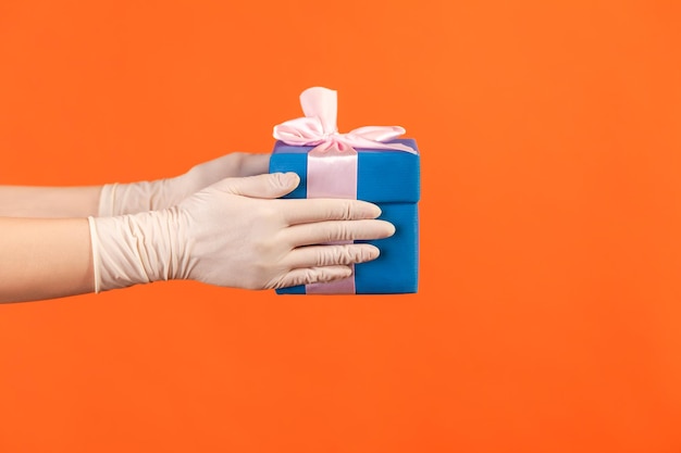 Mano humana en guantes quirúrgicos blancos con caja de regalo azul. concepto de compartir, dar o entregar