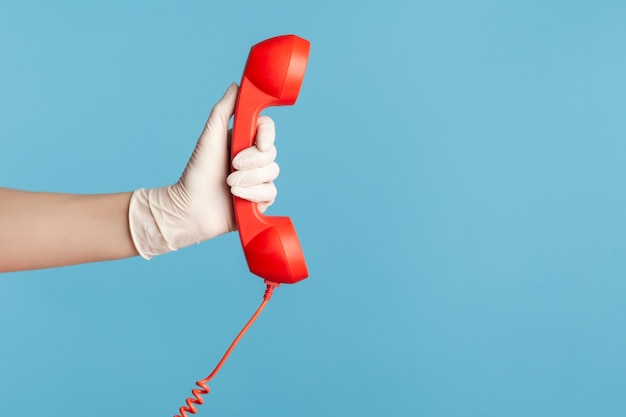 Mano humana en guantes quirúrgicos blancos sosteniendo y mostrando el auricular del teléfono cale rojo.