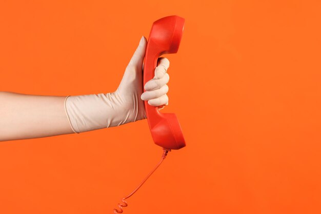 Foto mano humana en guantes quirúrgicos blancos sosteniendo y mostrando el receptor del teléfono de llamada roja.