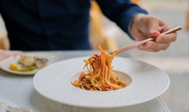 mano humana que eleva el udon a las verduras con palillos