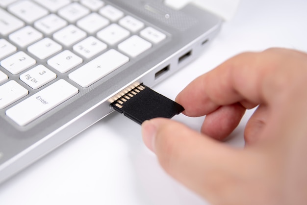 Foto mano humana que enchufa una tarjeta de medios sd en la computadora portátil personal en blanco.