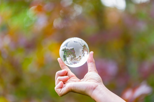 Foto mano humana sosteniendo globo planeta vidrio en bosque verde con luces de naturaleza bokeh concepto del día mundial del medio ambiente para la conservación del medio ambiente proteger la ecología la tierra y la vida ecológica ambiental