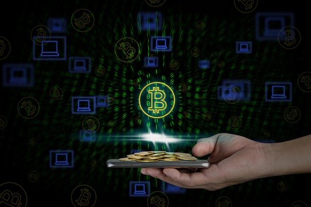 Mano humana sosteniendo un teléfono inteligente móvil con pilas de monedas y símbolo de bitcoin en fondo binario