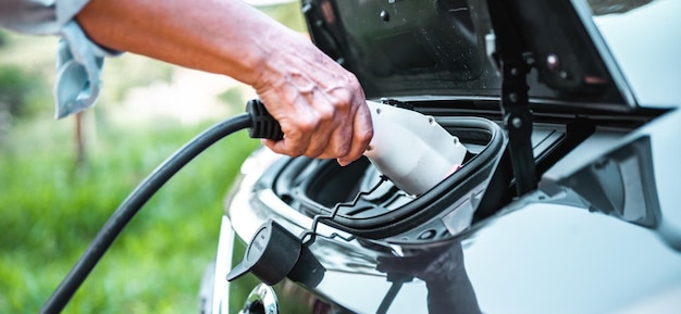 La mano humana sostiene la conexión de carga del coche eléctrico al coche eléctrico