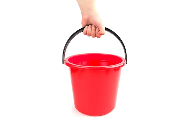 Una mano humana sostiene un cubo de agua de plástico rojo sobre un fondo blanco.