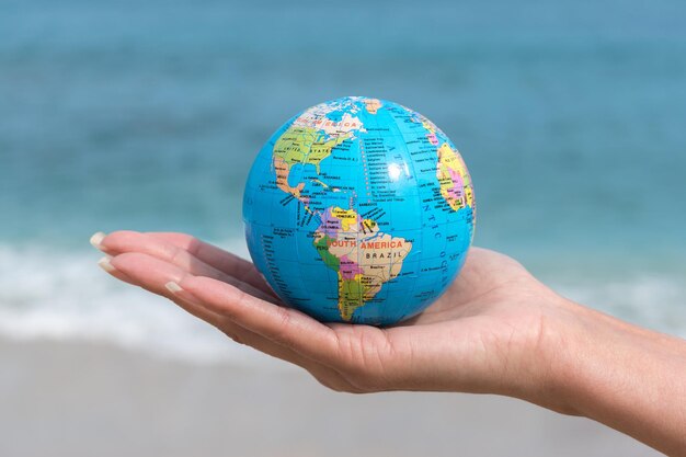 La mano humana sostiene un pequeño globo frente al mar.