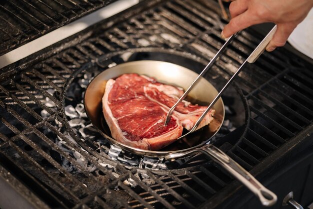 Mano humana usando pinzas para asar a la parrilla para voltear el bistec en la parrilla al aire libre