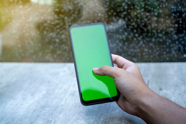 Foto mano humana usando un teléfono móvil con una pantalla en blanco con una ventana clara y fondo de gota de lluvia pantalla en blanco para copiar espacio