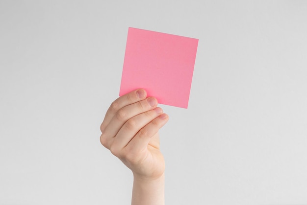 Mano infantil sosteniendo un recordatorio cuadrado rosa en blanco o notas de papel sobre un fondo blanco y gris