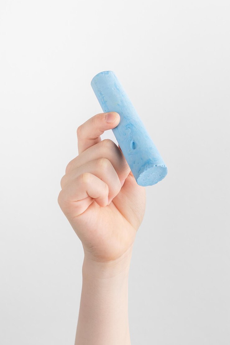 Foto mano infantil sosteniendo un trozo de tiza azul con fondo blanco y gris con espacio para copiar