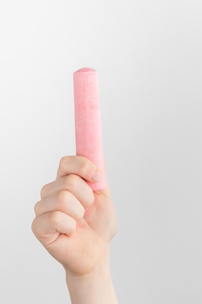 Mano infantil sosteniendo un trozo de tiza rosa con fondo blanco y gris con espacio para copiar