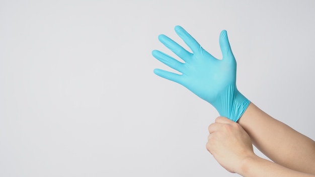 La mano izquierda está tirando de la mano derecha con guantes de látex azul sobre fondo blanco.