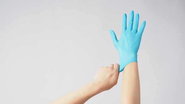 La mano izquierda está tirando de la mano derecha con guantes de látex azul sobre fondo blanco.