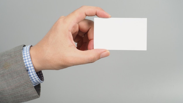 La mano izquierda sostiene una tarjeta blanca en blanco y usa un traje sobre fondo gris. concepto de hombre de negocios