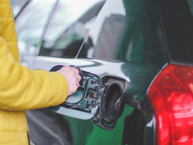 La mano de un joven caucásico con una chaqueta amarilla desenrosca la tapa del tanque de combustible