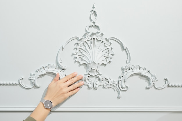 Mano de joven clienta elegante de estudio contemporáneo de diseño de interiores tocando el ornamento en la pared blanca mientras elige uno para su piso