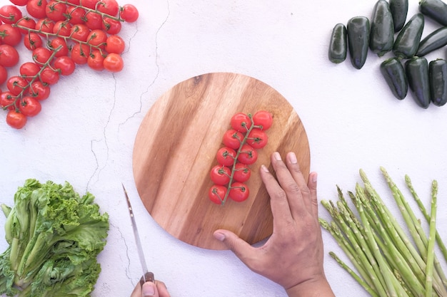 Mano joven cortando tomate cherry de color rojo en una tabla de cortar