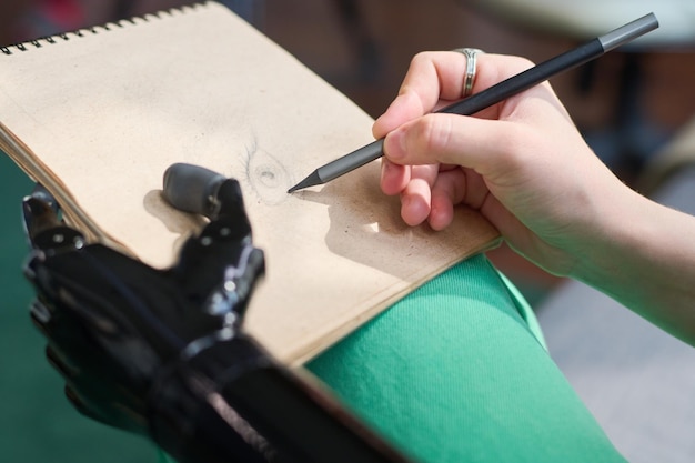 Mano de una joven diseñadora con prótesis dibujando un ojo en la página del bloc de notas