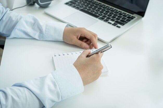 La mano de la joven empresaria asiática toma nota y trabaja en línea desde su oficina en casa, el concepto de enseñanza de distanciamiento social durante las enfermedades por virus COVID.