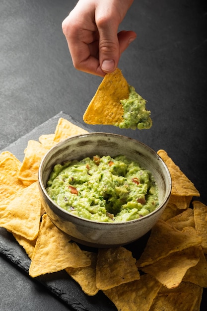 La mano del joven está recogiendo un poco de salsa de guacamole con chips de nachos Comida saludable de verduras veganas