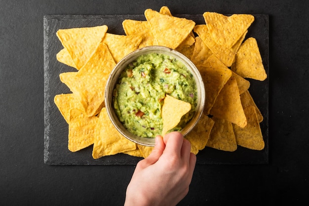 La mano del joven está recogiendo un poco de salsa de guacamole con chips de nachos Comida saludable de verduras veganas