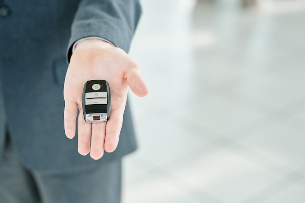 Mano del joven gerente contemporáneo del centro automático que sostiene el sistema de alarma de control remoto mientras se lo pasa al cliente que compra un automóvil nuevo