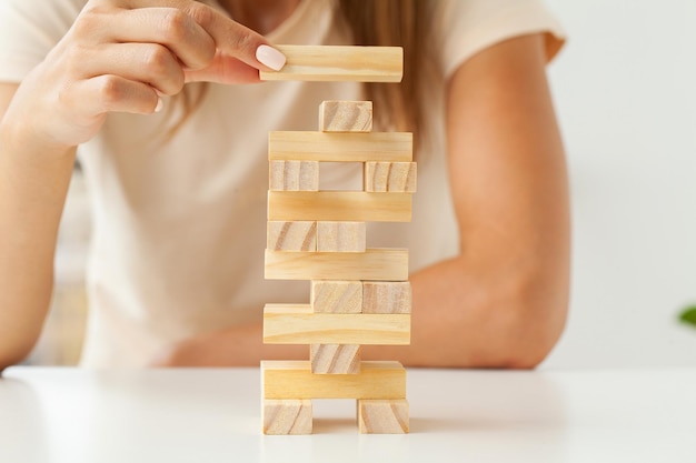 Mano de una joven mujer de negocios para jugar al juego de bloques de madera con estrategia y gestión sistemática de proyectos empresariales